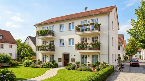 Gepflegtes Mehrfamilienhaus mit hellem Putz, neuen Fenstern und begrünten Balkonen.